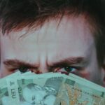 serious young male covering face with banknotes